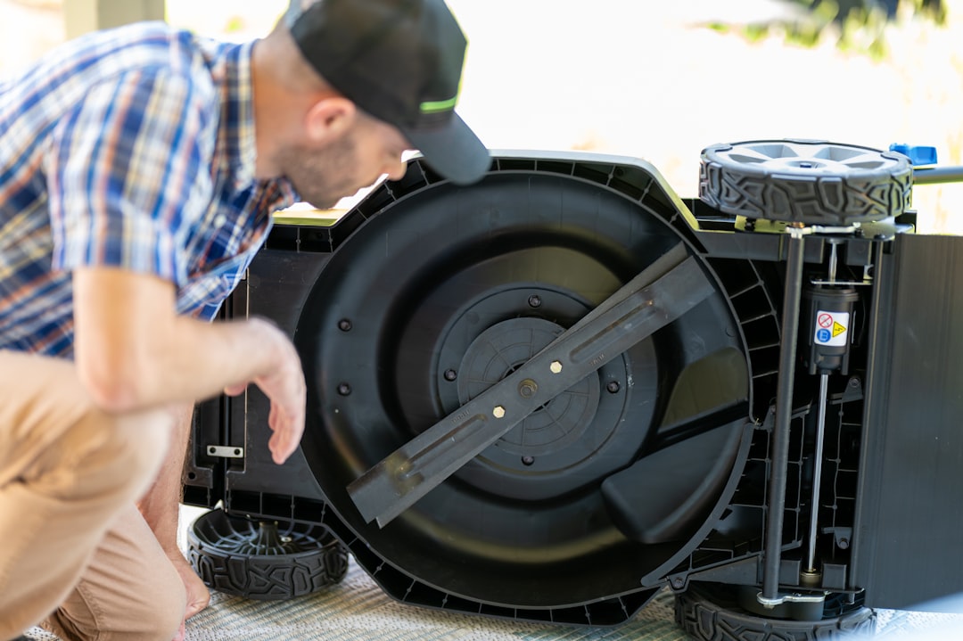 Man examining the underside of a lawn mower.