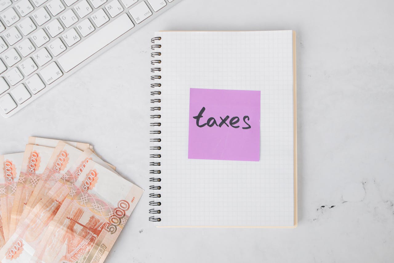 Flat lay image of tax preparation, featuring cash, a notebook, and a computer keyboard on a white surface.